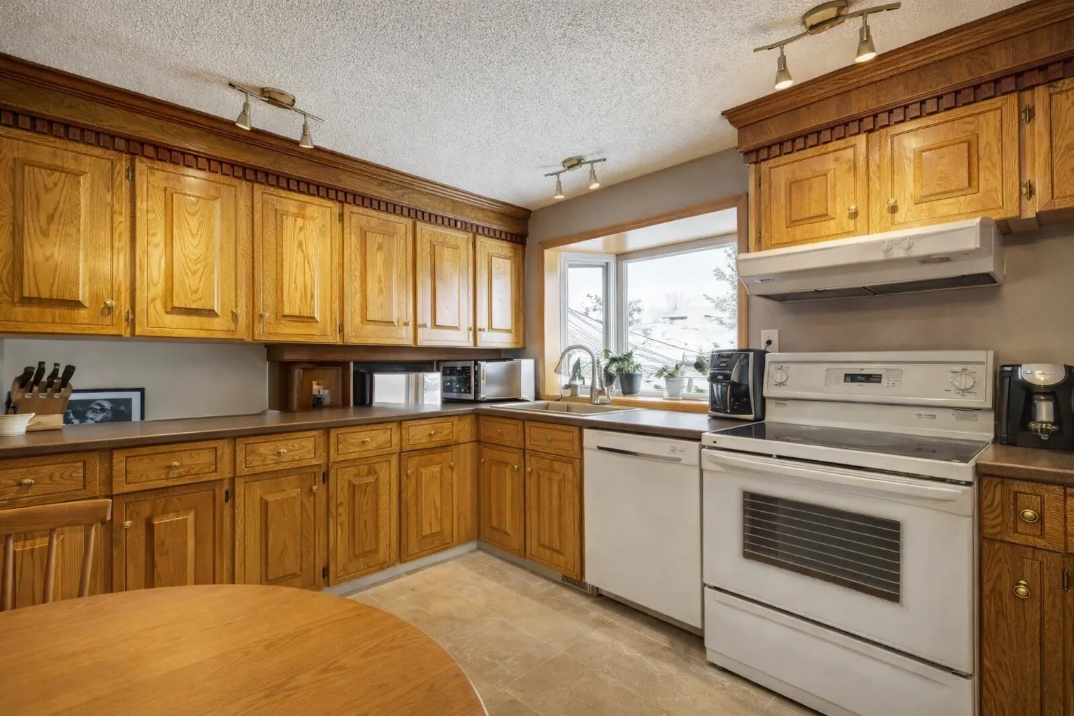 Before photo of an outdated Calgary kitchen with old oak cabinetry and white appliances prior to remodeling